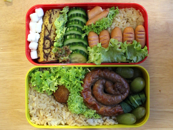Bento Box gefüllt mit Reis, Würstchen, Bratwurst, Banane, Marshmallows, Weintrauben, Käse, Falafel. Alles angeordnet im Indiana Jones Thema.