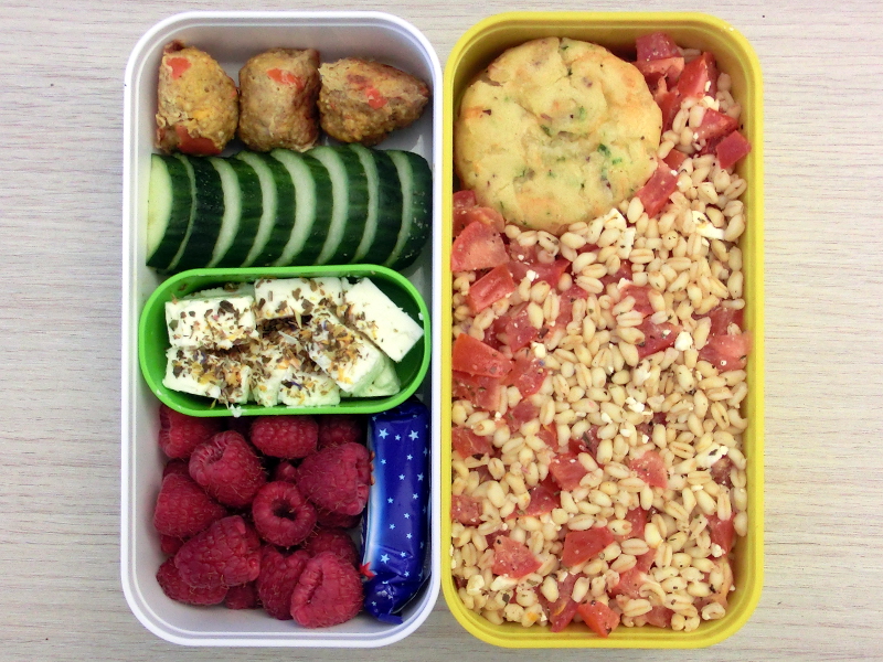 Bento Box gefüllt mit Weichweizen-Tomaten Salat, Muffin, Hackbällchen, Gurke, Schafskäse, Himbeeren, Schokolade