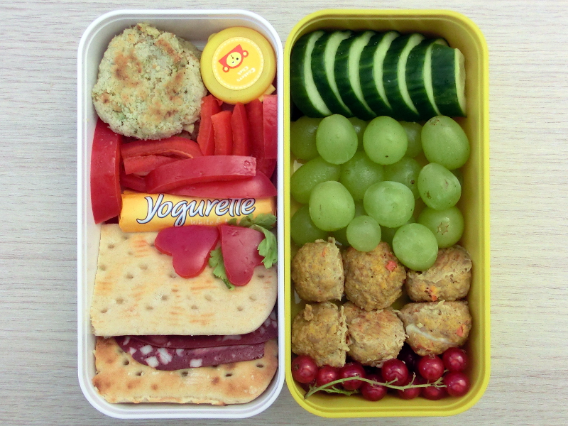 Bento Box gefüllt mit Gemüsebratlinge, Paprika, Schokolade, Brot mit Aufschnitt, Gurke, Weintrauben, Hackbällchen, Johanissbeeren