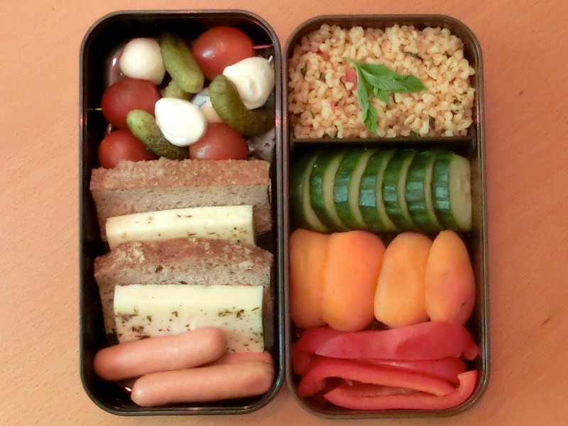Bento Box gefüllt mit Würstchen, Käse, Tomate-Mozzarella Spieße, Cous Cous, Gurke, Aprikosen, Paprika