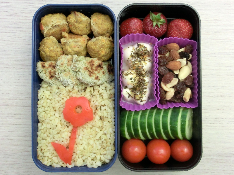 Bento Box gefüllt mit Hackbällchen, Gemüsebratlinge, Cous Cous, Paprika, Erdbeeren, Mozzarella, Studentenfutter, Gurke, Tomaten
