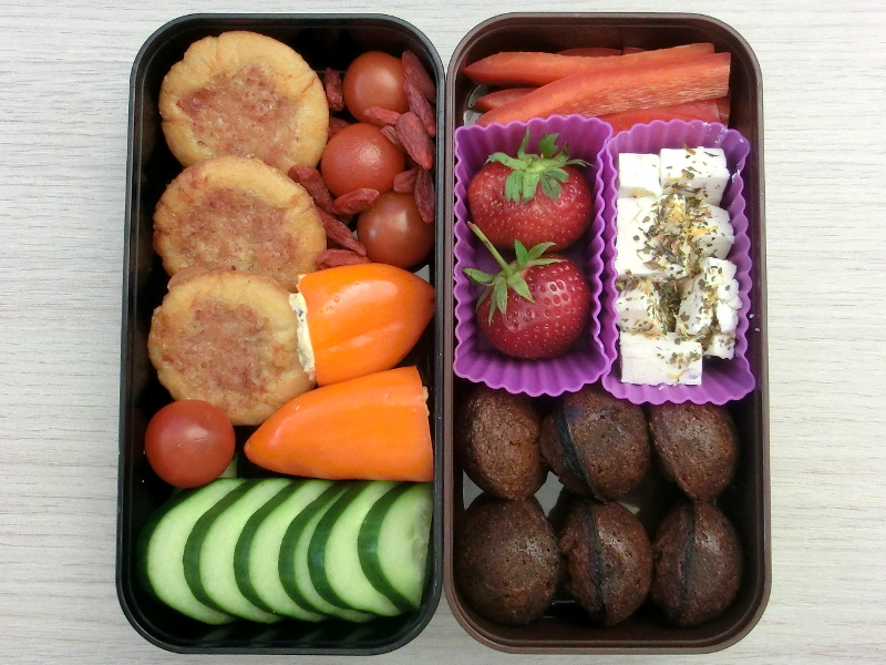 Bento Box gefüllt mit Paprika, Tomaten, Gojibeeren, Käse-Schinken-Pies, Gurke, Erdbeeren, Schafskäse, Browniekugeln