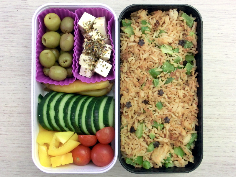 Bento Box gefüllt mit Reispfanne, Oliven, Schafskäse, Peperoni, Gurke, Paprika, Tomaten