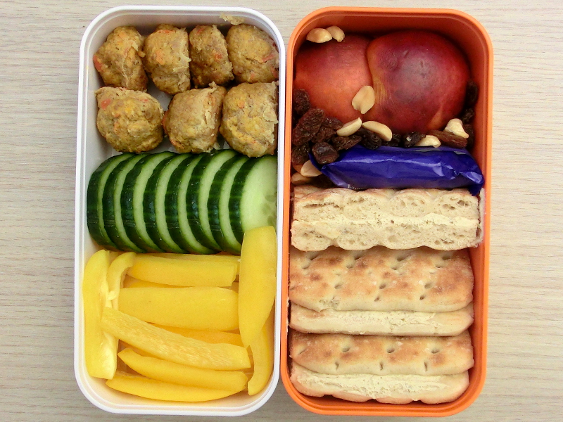 Bento Box gefüllt mit Brot mit Olivencreme, Schokolade, Studentenfutter, Nektarine, Hackbällchen, Gurke, Paprika