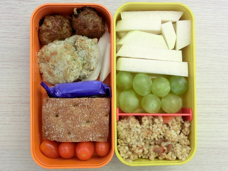 Bento Box gefüllt mit Bulgur, Weintrauben, Kohlrabi, Hackbällchen, Gemüsebratling, Schokolade, Brot, Tomaten