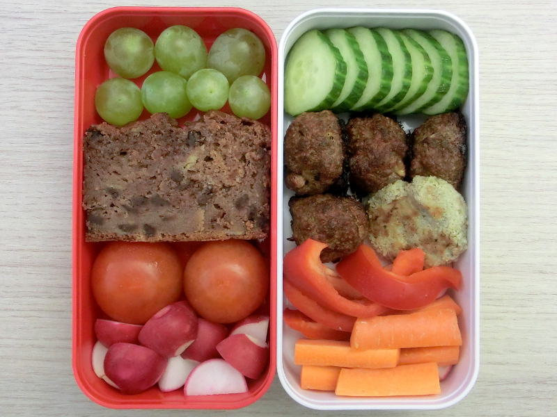 Bento Box gefüllt mit Gemüsebratling, Hackbällchen, Paprika, Möhren, Gurke, Weintrauben, Banane-Schoko-Kuchen, Tomaten, Radieschen