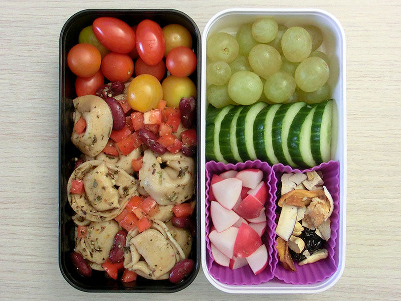 Bento Box gefüllt mit Tortellini, Tomaten, Radieschen, Trockenobst, Gurke, Weintrau