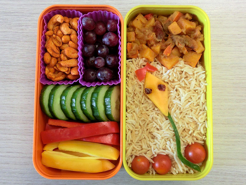 Bento Box gefüllt mit Kürbis-Salat, Reis, Paprika, Erdnüsse, Weintrauben, Tomaten, Gurke