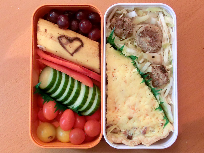 Bento Box gefüllt mit Selbstgemachter Krautsalat, Hackbällchen, Quiche, Paprika, Gurke, Tomaten, Weintrauben, Banane