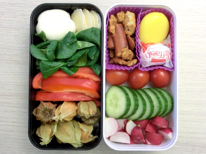 Bento Box gefüllt mit Gurke, Tomaten, Radieschen, Raffaello, Babybel, Pretzels, Ei, Parmesancracker, Paprika, Physalis