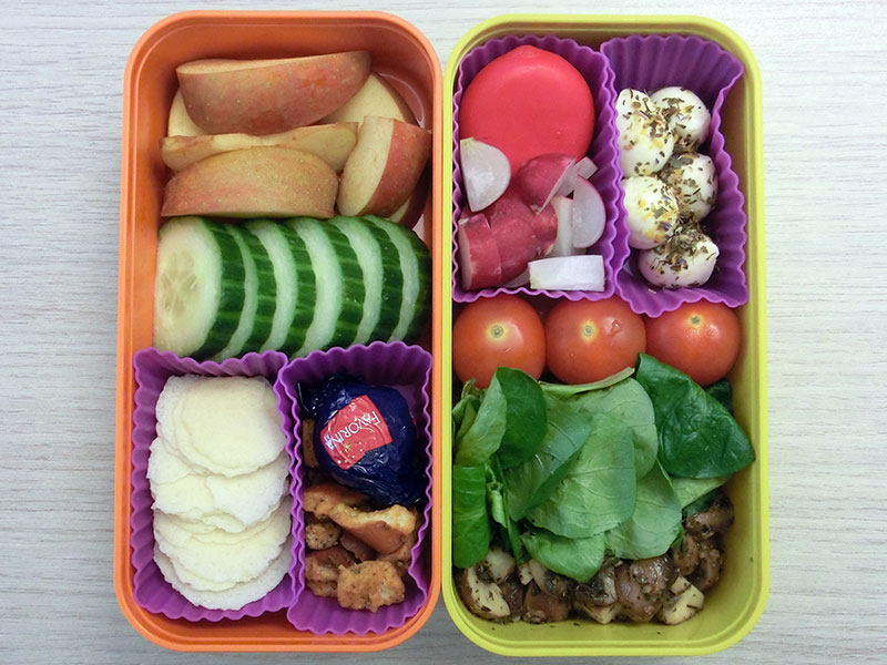 Bento Box gefüllt mit Apfel, Gurke, Parmesan Cracker, Pretzels, Schokolade, Pilze, Tomaten, Morzarella, Radieschen, Babybel