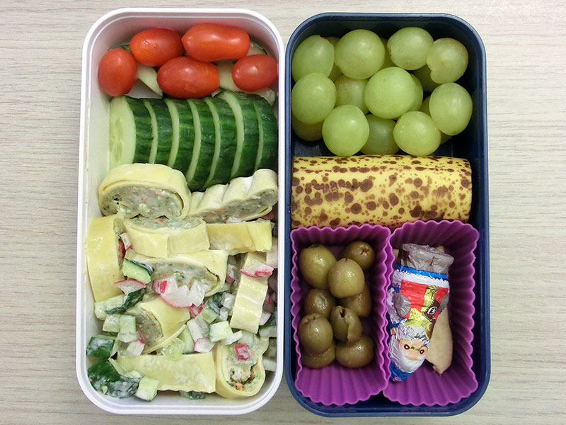 Bento Box gefüllt mit Maultaschensalat, Gurke, Tomaten, Oliven, Schokolade, Banane, Weintrauben