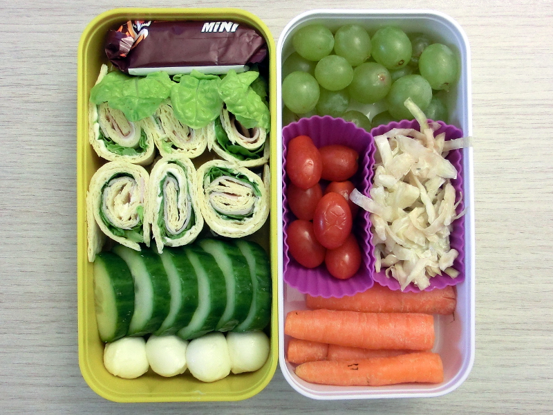 Bento Box gefüllt mit Wraps, Gurke, Schokolade, Mozzarella, Weintrauben, Tomaten, Salat, Möhren