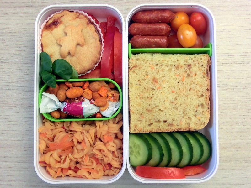 Bento Box gefüllt mit Pastete, Paprika, Nüsse, Nudeln, Cabanossi, Tomaten, Sandwich, Gurke