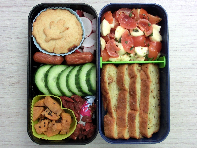 Bento Box gefüllt mit Tomate-Mozzarella, Brot, Auflauf, Radieschen, Cabanossi, Süßkartoffeln, Goji-Beeren, Schokolade