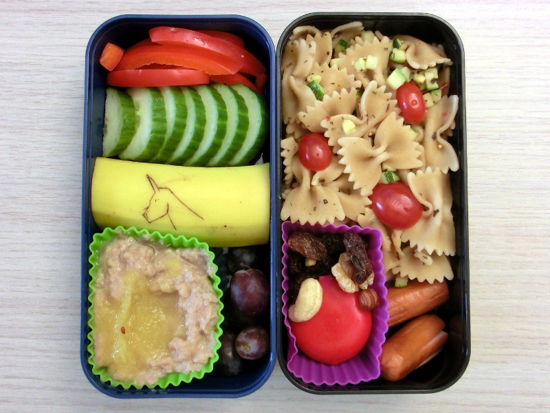 Bento Box gefüllt mit Paprika, Gurke, Banane, Grießbrei, Weintrauben, Nudeln, Babybel, Studentenfutter, Würstchen