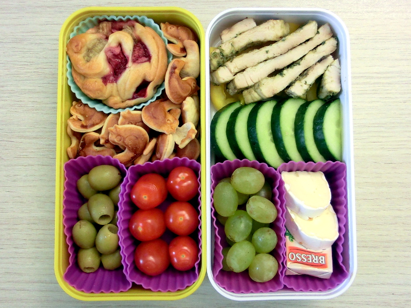 Bento Box gefüllt mit Gurke, Paprika, Putenschnitzel, Weintrauben, Käse, Rhabarbermuffin, Kekse, Oliven, Tomaten