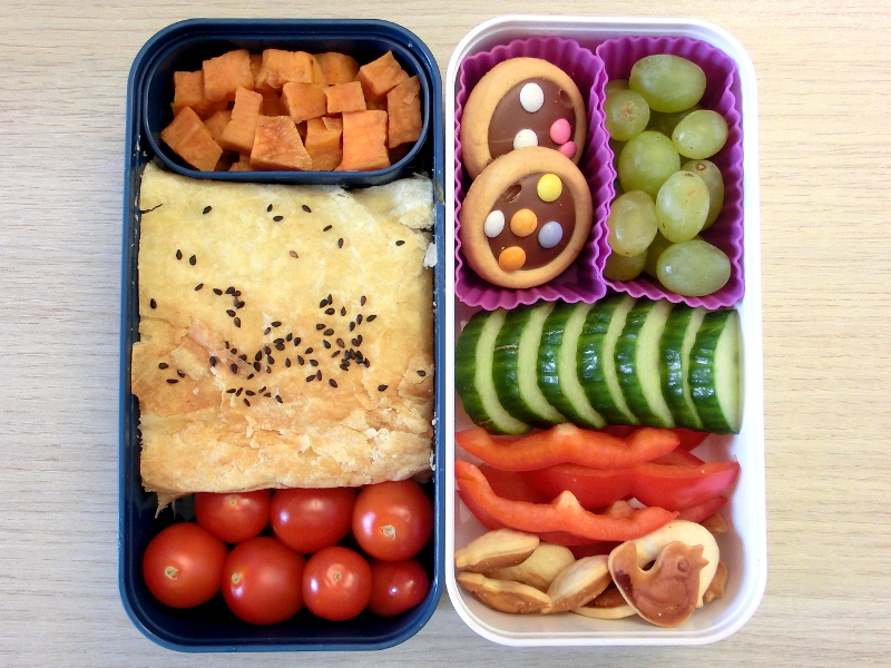 Bento Box gefüllt mit Kekse, Paprika, Gurke, Weintrauben, Börek, Süsskartoffeln, Tomate