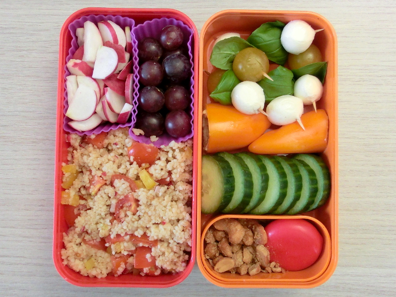 Bento Box gefüllt mit Cous cous, Radieschen, Weintrauben, Erdnüsse, Babybel, Gurke, Paprika, Tomate-Morzarella