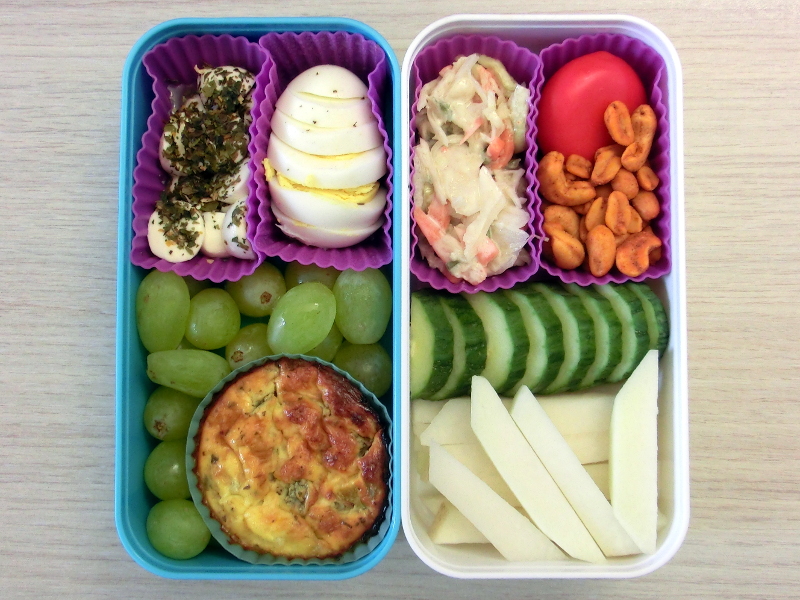 Bento Box gefüllt mit Ei, Morzarella, Weintrauben, Quiche, Cole Slaw, Erdnüsse, Babybel, Gurke, Kolrabi