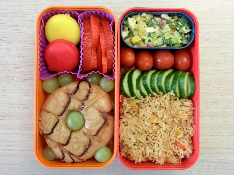 Bento Box gefüllt mit Reis, Gurke, Tomaten, Kartoffelsalat, Donut, Weintrauben, Paprika, Babybel
