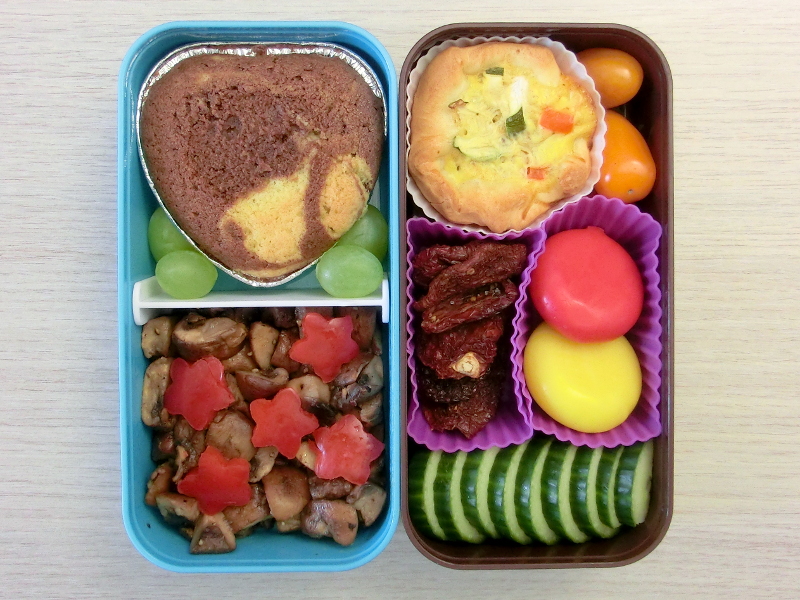 Bento Box gefüllt mit Gurke, Getrocknete Tomaten, Babybel, Tomaten, Quiche, Kuchen, Weintrauben, Champignons