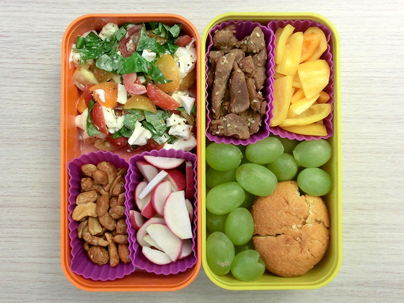 Bento Box gefüllt mit Tomaten-Mozarella, Erdnüsse, Radieschen, Weintrauben, Muffin, Hühnchen, Paprika