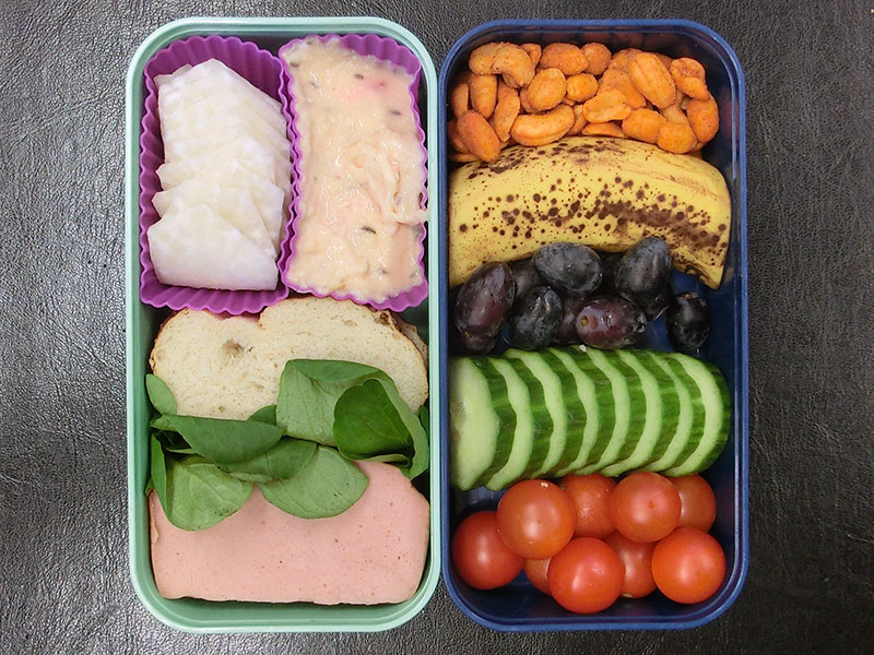 Bento Box gefüllt mit Leberkäse, Laugenbrot, Obazta, Rettich, Erdnüsse, Banane, Weintrauben, Gurke, Tomaten