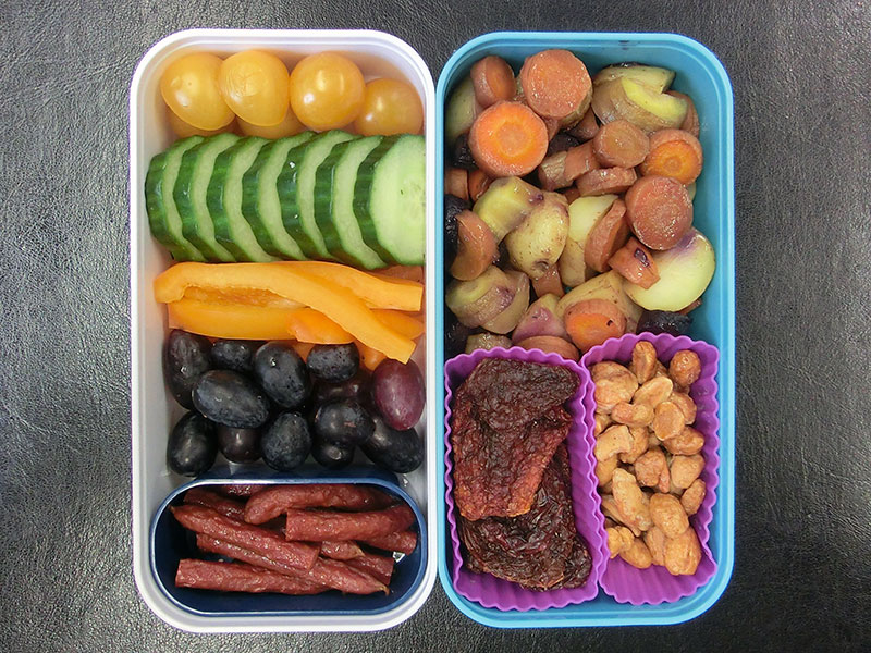 Bento Box gefüllt mit Weintrauben, Salami, Paprika, Gurke, Tomaten, Gemüsepfanne, Getrocknete Tomaten, Erdnüsse