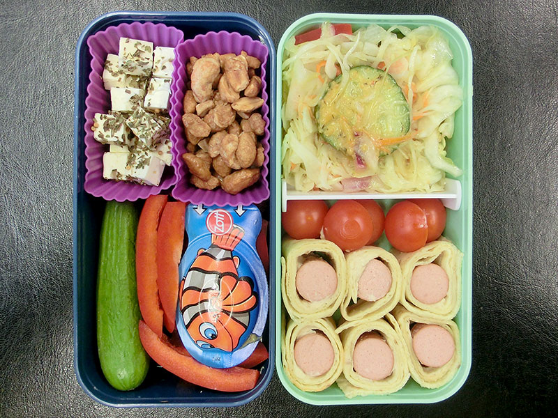 Bento Box gefüllt mit Wraps mit Würstchen, Tomaten, Salat, Erdnüsse, Käse, Gurke, Paprika, Schafskäse