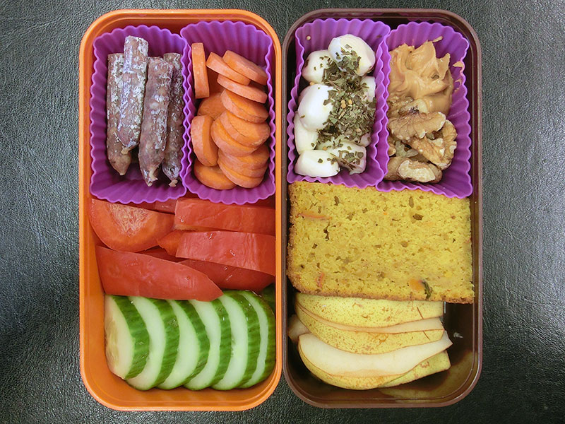 Bento Box gefüllt mit Nüsse, Erdnussbutter, Kürbisbrot, Mozzarella, Birne, Möhren, Salami, Paprika, Gurke