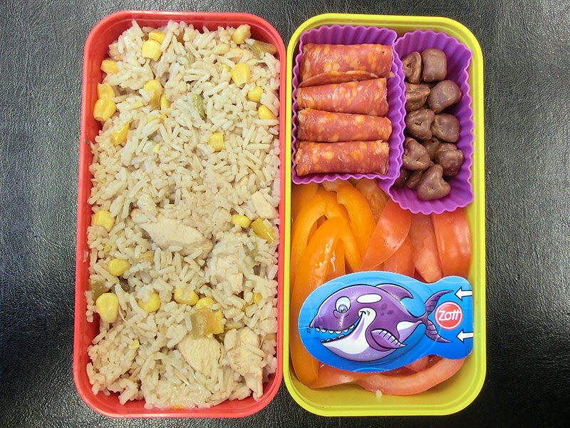 Bento Box gefüllt mit Geflügel-Reis-Pfanne, Salami, Schokolade, Paprika, Tomaten, Käse