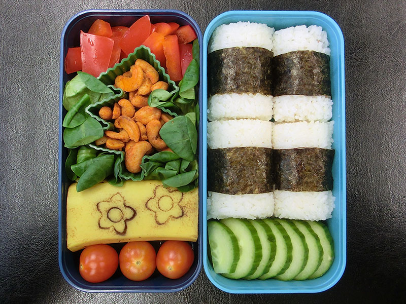 Bento Box gefüllt mit Gurke, Lachssushi, Tomaten, Banane, Nüsse, Paprika