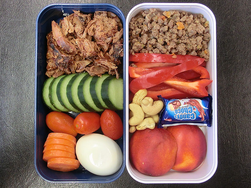 Bento Box gefüllt mit Pulled Pork, Beef Tea, Tomaten, Gurke, Ei, Karotte, Paprika, Nüsse, Schokolade, Aprikose