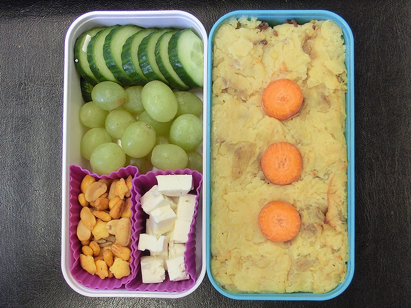 Bento Box gefüllt mit Kartoffelmus, Gurke, Weintrauben, Nüsse, Schafskäse